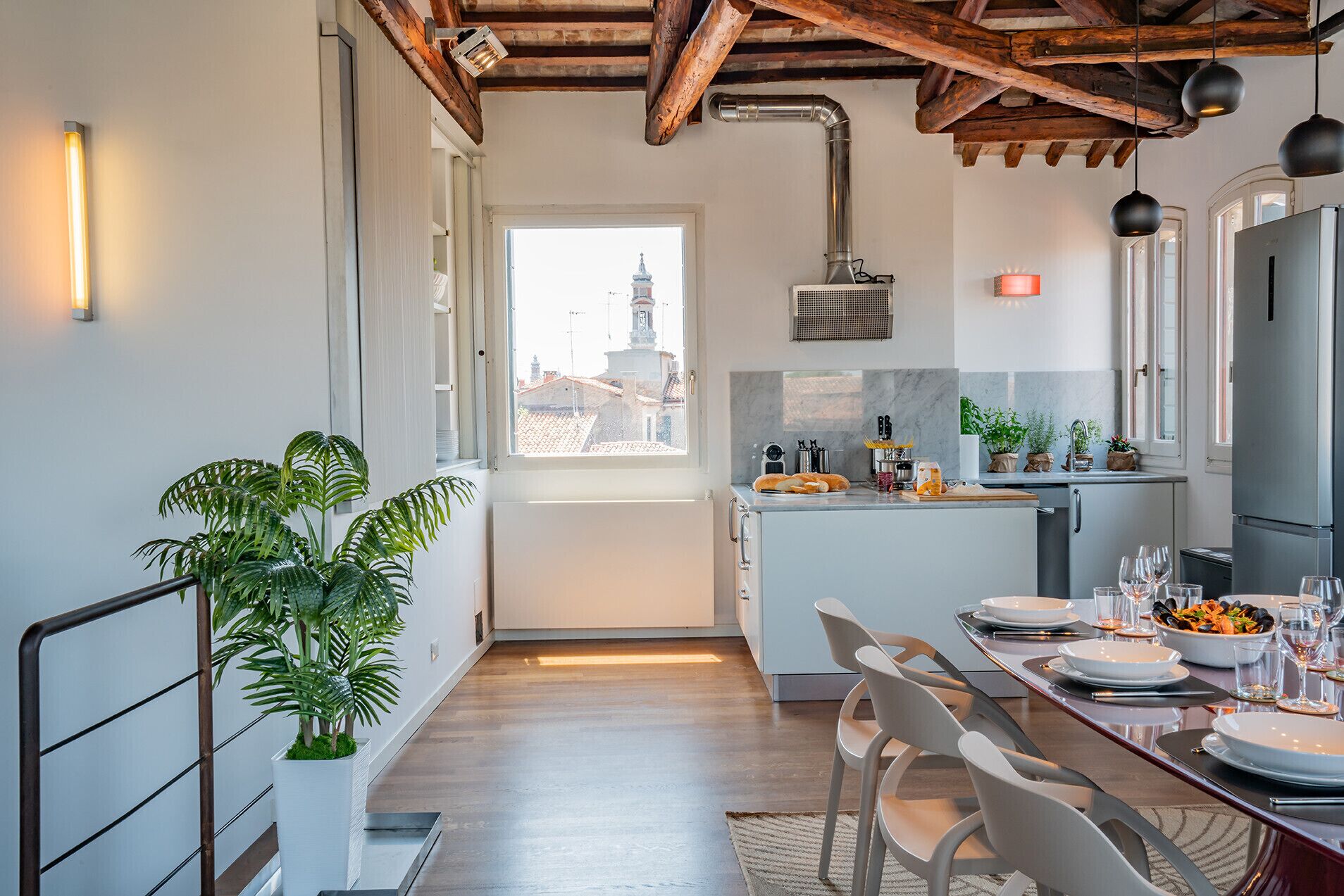 A modern kitchen with a central island, a dining area with chairs, and a view of buildings outside.