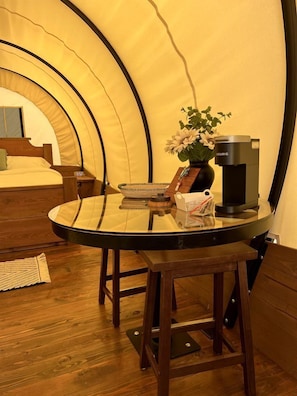 A cozy room with a bed, a round table with a coffee maker, and a potted plant.