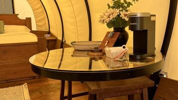 Una habitación acogedora con una cama, una mesa redonda con cafetera y una planta en maceta.