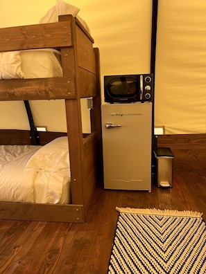 A bunk bed with a microwave and a small refrigerator in a room with wooden flooring and a patterned rug.