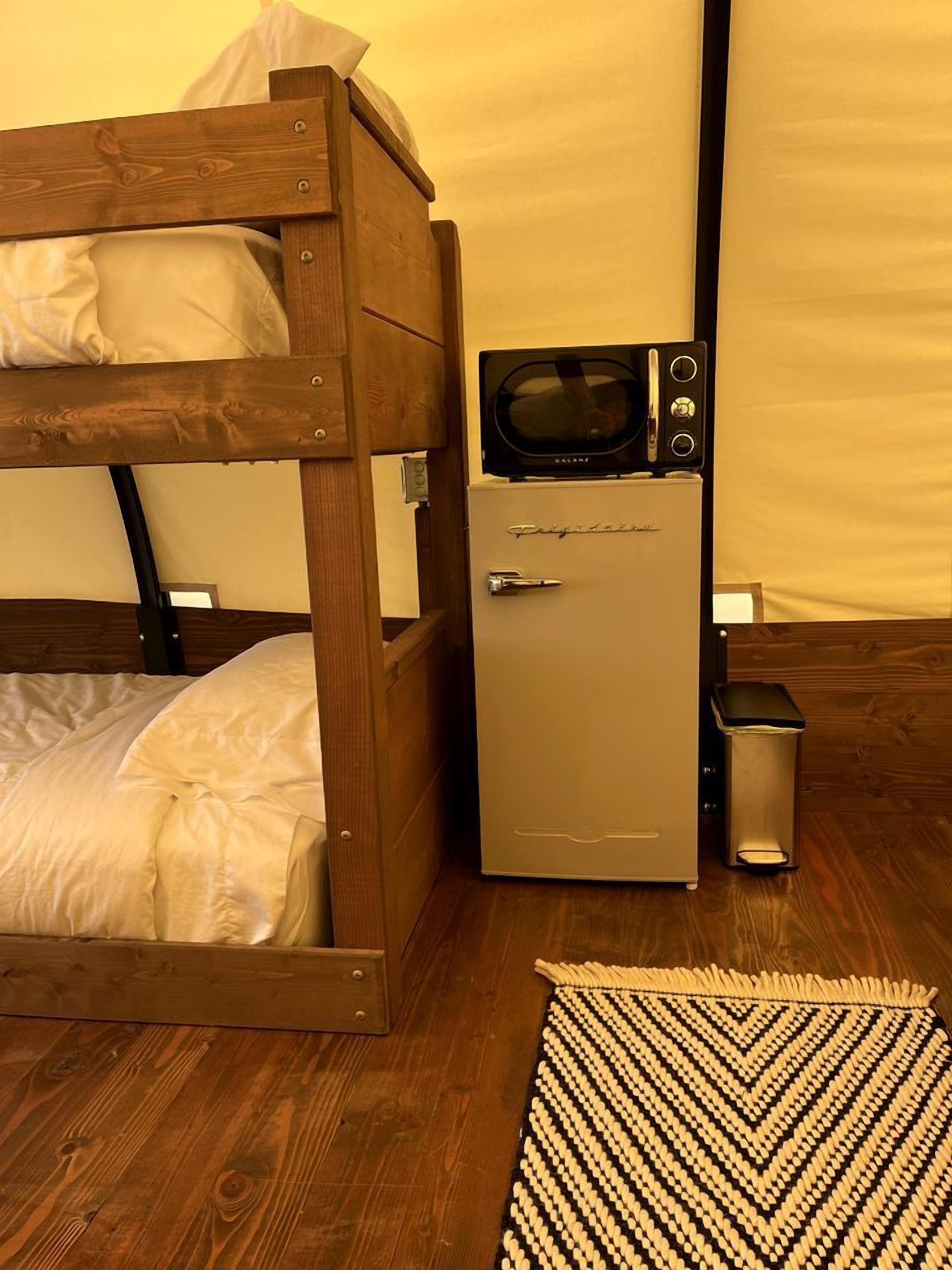 Een stapelbed met een magnetron en een kleine koelkast in een kamer met houten vloeren en een kamerbreed tapijt met dessin.