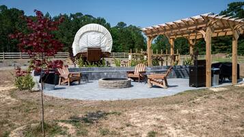 An outdoor patio area with a wooden pergola, seating, a fire pit, and a covered structure.