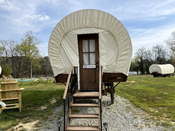 A covered wagon with a wooden door, a sign reading 'Wild Blue,' and a wooden staircase leading up to it.