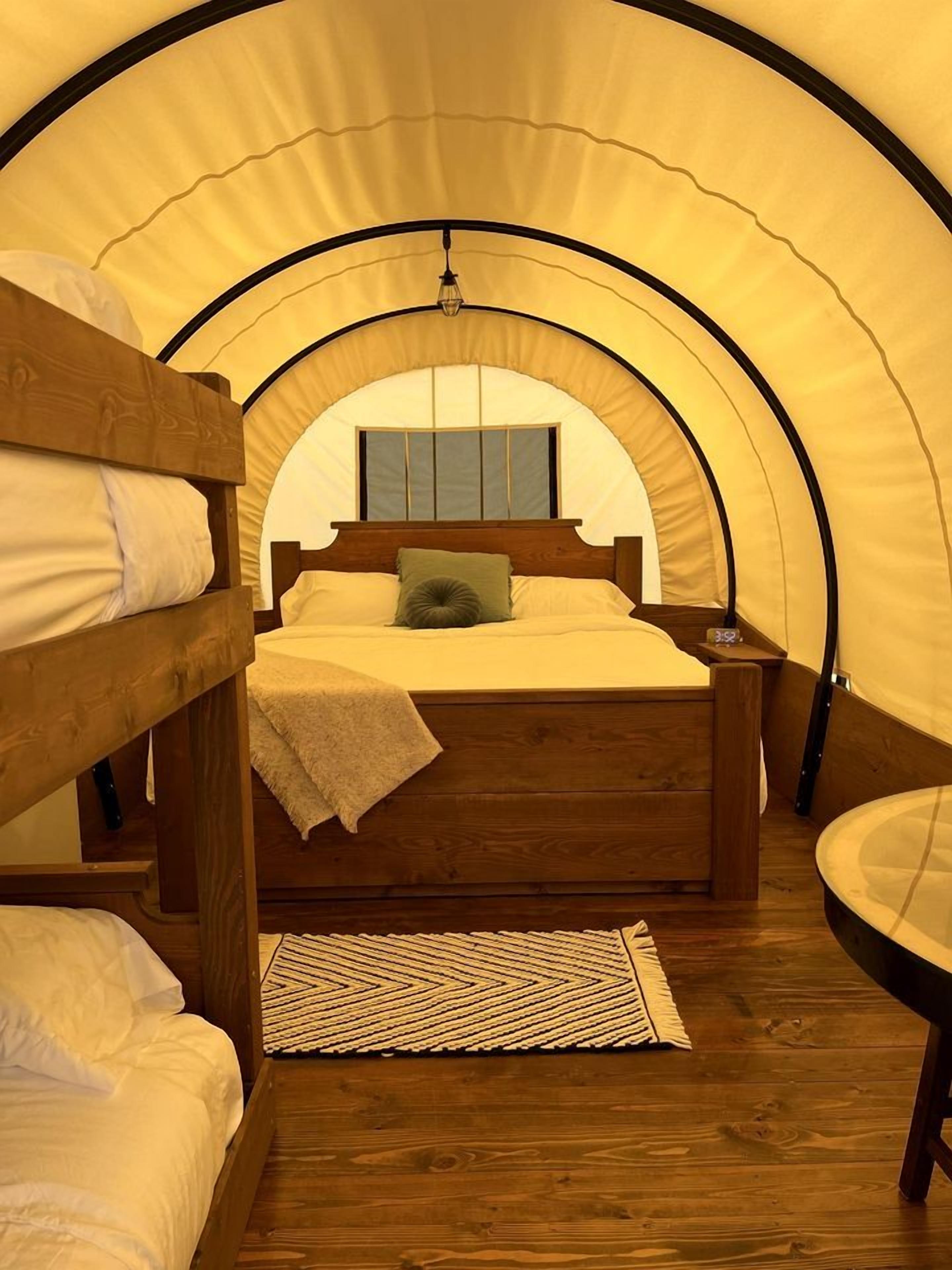 A tented accommodation with a bunk bed, a bedside table, and a small round table.