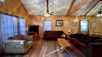 A wooden-paneled room with a sofa, a loveseat, a coffee table, and a television.