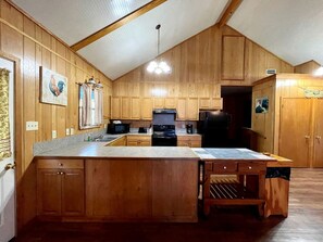 Eine Holz-Küche mit einer zentralen Kochinsel, Holzsäcken und einem schwarzen Herd und einem Kühlschrank.