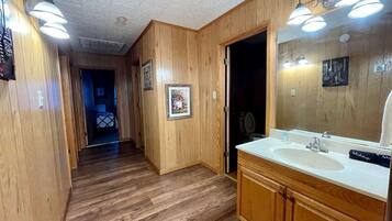 A wooden-paneled hallway leading to a bathroom with a sink, mirror, and vanity.