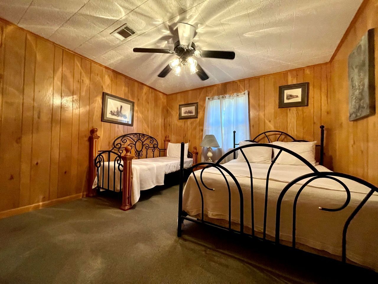 A bedroom with two beds, wooden walls, a ceiling fan, and framed pictures.