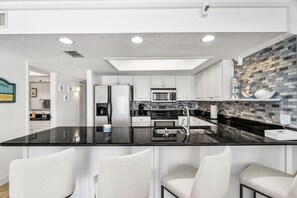 Une cuisine moderne dotée d’un îlot central, d’appareils électroménagers en acier inoxydable et d’un revêtement mural décoré de motifs en mosaïque.