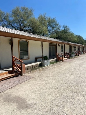 A row of motel rooms with individual entrances, outdoor seating, and a gravel driveway.