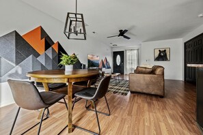 Un salon moderne avec une table à manger en bois, des chaises noires, un canapé marron et un ventilateur de plafond.