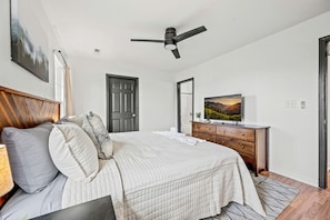 Une chambre à coucher avec un lit, une commode, un ventilateur de plafond, une télévision et une porte.