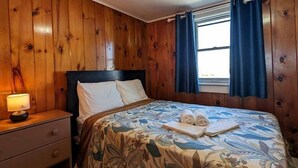 Ein Zimmer mit Holzwänden, einem Bett, einem Nachttisch und einem Fenster mit Vorhängen.