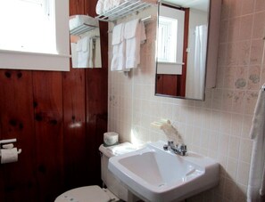 A bathroom with a wooden wall, a white sink, a toilet, and a mirror. - Beachfront Cottages with Private Access & Ocean Views in North Truro, Massachusetts (North Truro)
