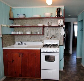 A kitchen with a white stove, a sink, wooden cabinets, and a countertop with various dishes and utensils. - Beachfront Cottages with Private Access & Ocean Views in North Truro, Massachusetts (North Truro)