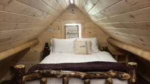 A cozy attic bedroom with a wooden bed frame, a window with a view, and a sign on the wall. - Peaceful Log Cabin Perfect for a Romantic Getaway near Yellowstone, Idaho (Island Park)