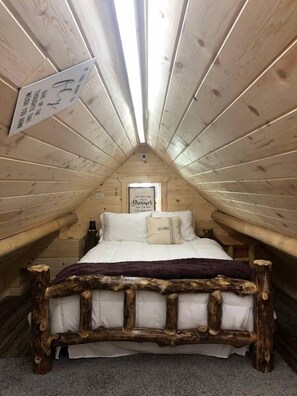 Ein gemütliches Schlafzimmer im Dachgeschoss mit Holzbettgestell, einem Fenster mit Blick und einem Schild an der Wand.