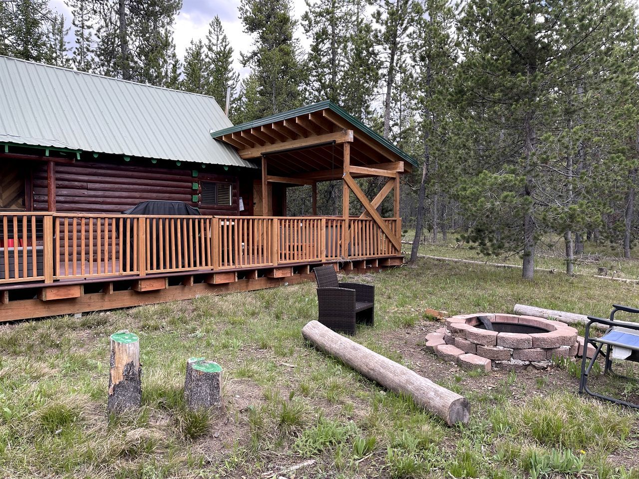 A log cabin with a wooden deck and a fire pit.