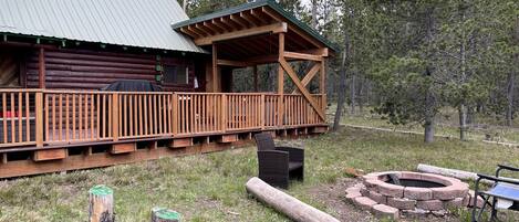 A log cabin with a wooden deck and a fire pit.