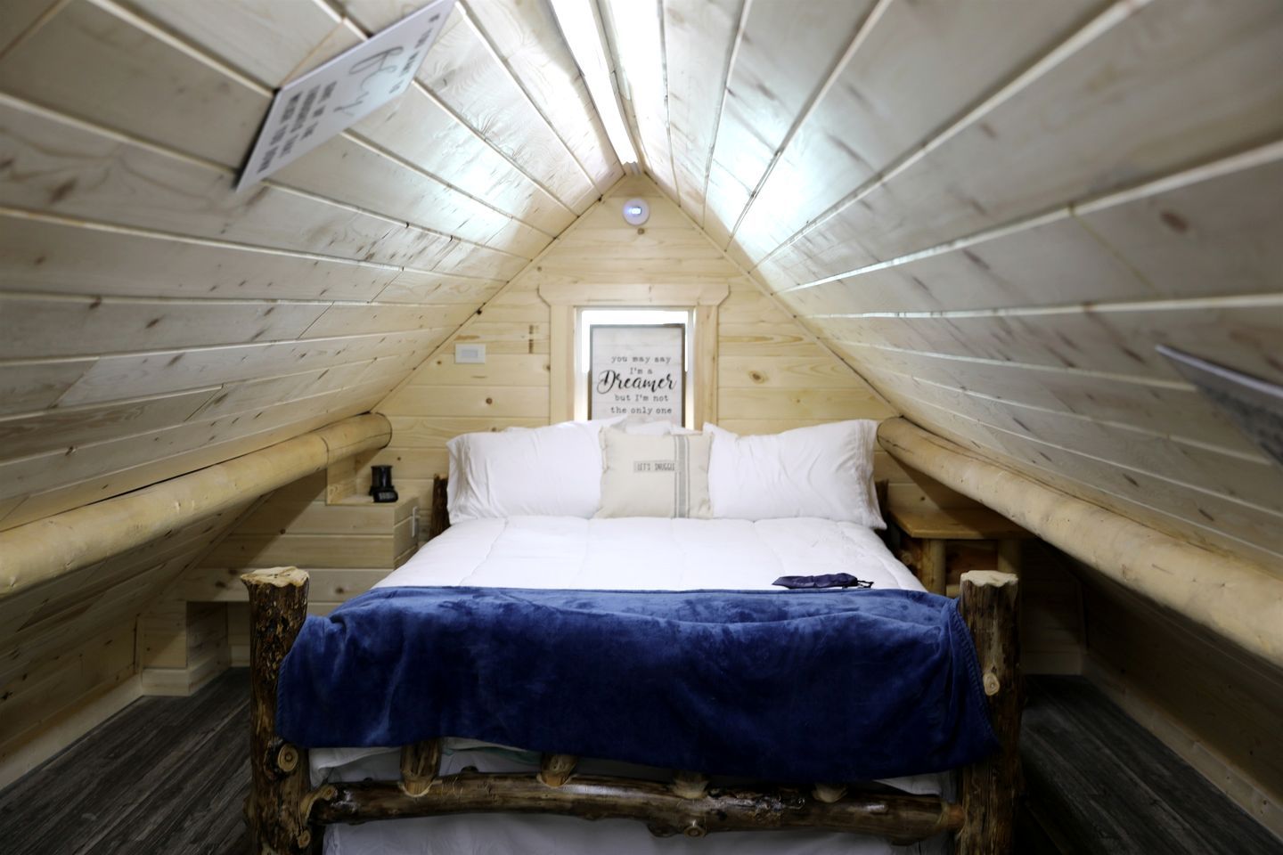 A cozy attic bedroom with a wooden bed, a nightstand, and a wall-mounted light fixture.