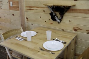 Ein Holztisch mit Tellern, Besteck und einer Tasse, vor einer Holzwand mit einem aufgehängten Tierkopf.