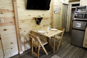 A wooden interior with a table, chairs, a TV, a microwave, and a refrigerator. - Peaceful Log Cabin Perfect for a Romantic Getaway near Yellowstone, Idaho (Island Park)