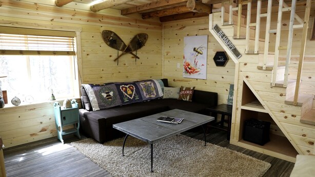 A cozy cabin interior with a wooden interior, a sofa, a coffee table, a small staircase, and a wall with decorative items. - Peaceful Log Cabin Perfect for a Romantic Getaway near Yellowstone, Idaho (Island Park)