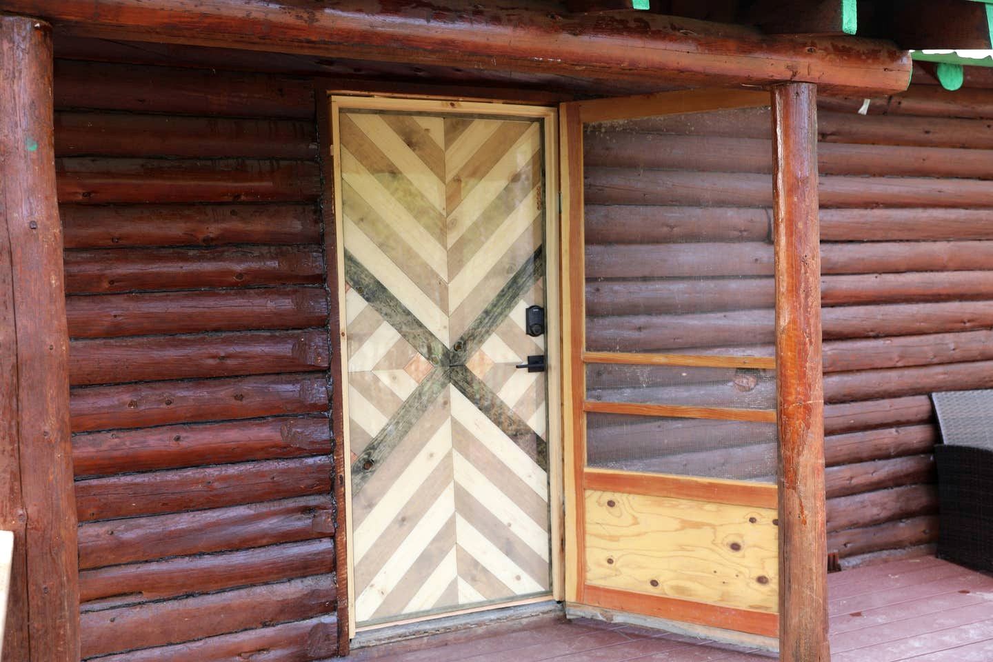 Een houten chalet met een deur in visgraatmotief, een klein terras en een zichtbaar raam.