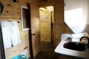 Innenansicht einer Holzhütte mit einem Badezimmer, das ein Waschbecken, einen Handtuchhalter und ein Schild mit der Aufschrift 'HAPPY PLACE' zeigt.