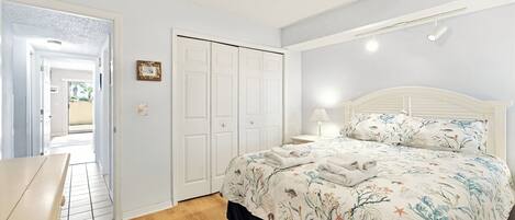 A bedroom with a bed, a nightstand, a lamp, a wardrobe, and a door leading to another room.