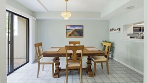 A dining area with a wooden table and chairs, a chandelier, a painting on the wall, and a kitchen area with a microwave. - Formal dining room, warm and inviting bedrooms, and a large screened porch! (St. Augustine Beach)