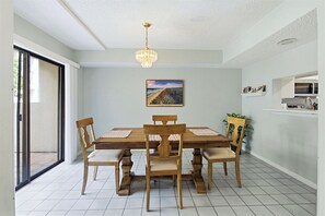 Ein Essbereich mit Holztisch und -stühlen, einer Kandelaber, einem Bild an der Wand und einer Küchenzeile mit einer Mikrowelle.