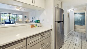 A modern kitchen with white cabinetry, a stainless steel refrigerator, and a tiled floor. - Formal dining room, warm and inviting bedrooms, and a large screened porch! (St. Augustine Beach)