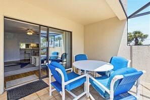 A balcony with a table and chairs, a sliding glass door leading to a kitchen, and a view of palm trees. - Formal dining room, warm and inviting bedrooms, and a large screened porch! (St. Augustine Beach)