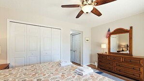 A bedroom with a bed, dresser, mirror, ceiling fan, and a door leading to another room. - Formal dining room, warm and inviting bedrooms, and a large screened porch! (St. Augustine Beach)