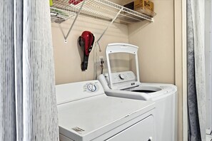 A laundry room with a white washing machine, a dryer, and a shelf above containing a red helmet and a box. - Formal dining room, warm and inviting bedrooms, and a large screened porch! (St. Augustine Beach)