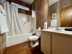 Un baño con bañera, inodoro y tocador con espejo.