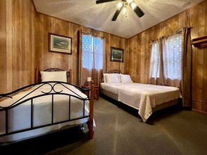 Ein Zimmer mit Holzwänden, einem Bett, einem Sessel, einem Nachttisch und einem Deckenventilator.