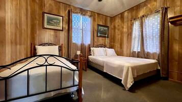 A room with wooden paneling, a bed, a chair, a nightstand, and a ceiling fan.