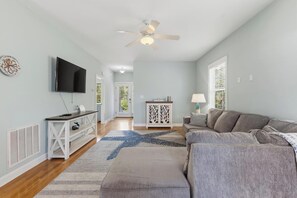 A living room with a TV, a ceiling fan, a sofa, a coffee table, and a decorative rug. - Joan and Eddie's Beach Retreat: Pet Friendly | Walking Distance to Beach (Carolina Beach)