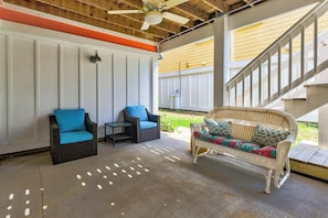 Ein überdachter Patio-Bereich mit Korbmöbeln, Deckenventilator und einer Treppe, die zu einer oberen Ebene führt.