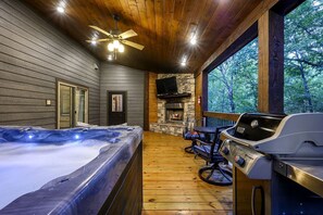 Ein Whirlpool, Sitzgelegenheiten im Freien, ein Grill und ein Kamin aus Stein in einer Holzhütte mit Holzwänden und einer Holzterrasse.