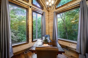 Eine Holzhütte mit großen Fenstern, einem Esstisch mit Blumen und einer Bank.