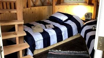 Interieur van een blokhut met een slaapverdieping, een houten trap en een raam met gordijnen.
