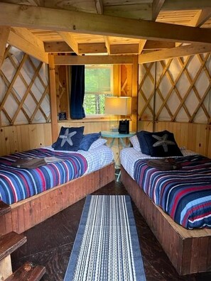 A cabin with two wooden beds, a small table, and a window with curtains.