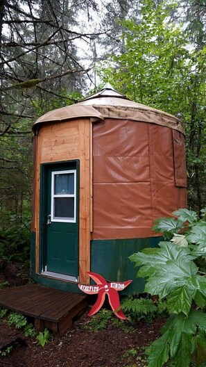 Een kleine, houten, koepelvormige constructie met een groene deur en een klein raam, omgeven door dicht bos.