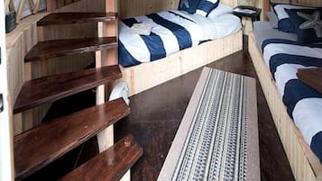 Eine Jurte mit Holzinnenraum, zwei Betten mit blauer Bettwäsche, einem Fenster und einer Holzleiter.