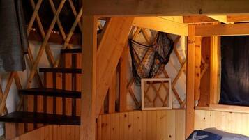 A wooden loft bedroom with a bunk bed, a ladder, and a small enclosed space with a netted window.