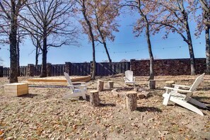An outdoor area with wooden chairs, a wooden bench, and a stone wall in the background. - Serene Woodland Studio Retreat with Outdoor Amenities, Near Fishing, Hiking & Gentry, AR (Gentry)