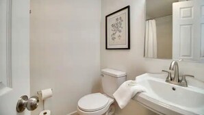A bathroom with a toilet, sink, and a framed picture on the wall.